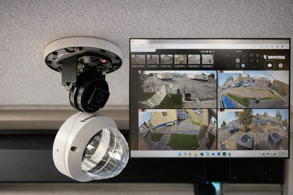 A Vivotek ceiling-mounted security camera alongside a monitor displaying a multi-view surveillance feed.