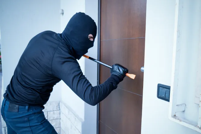 Masked intruder forcing a door, highlighting the need for a central burglar alarm to protect your property