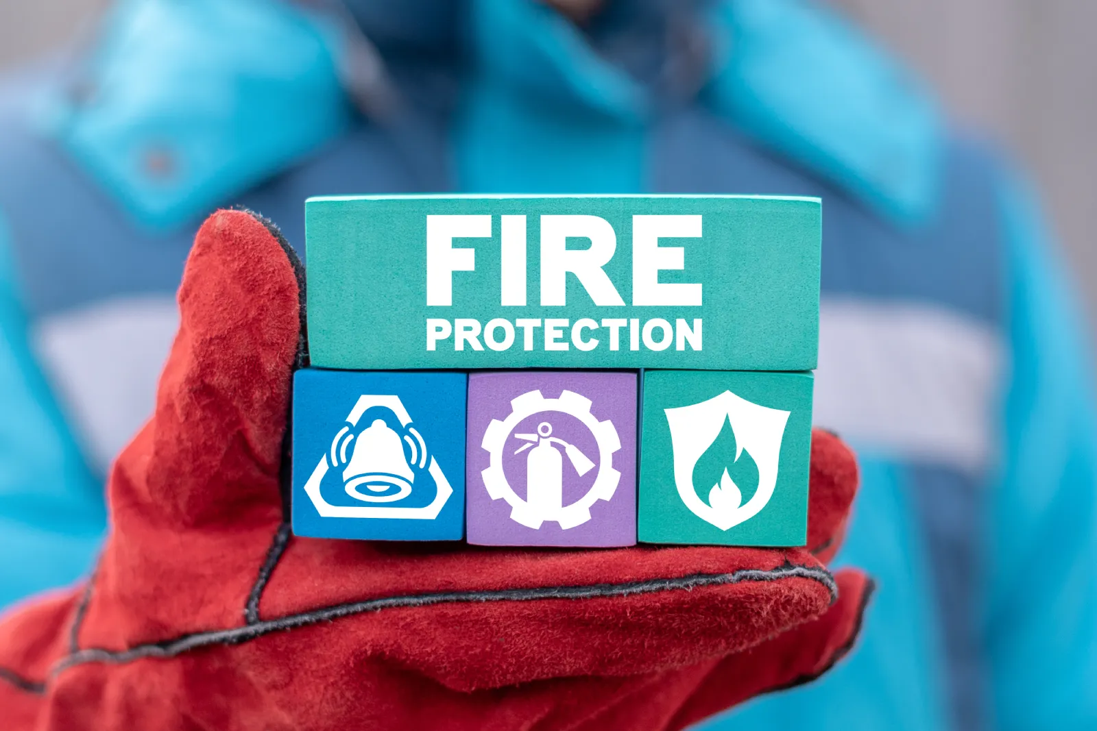 Firefighter holding blocks displaying fire protection systems icons including alarm, extinguisher, and flame shield