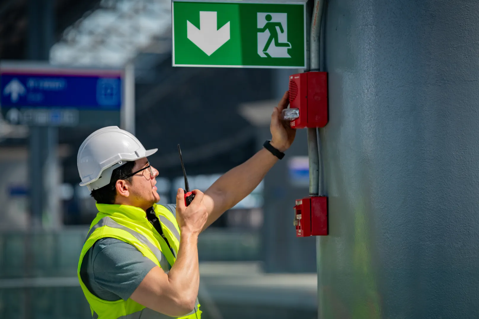 Technician inspecting fire alarm system requirements for Arizona businesses near an emergency exit sign
